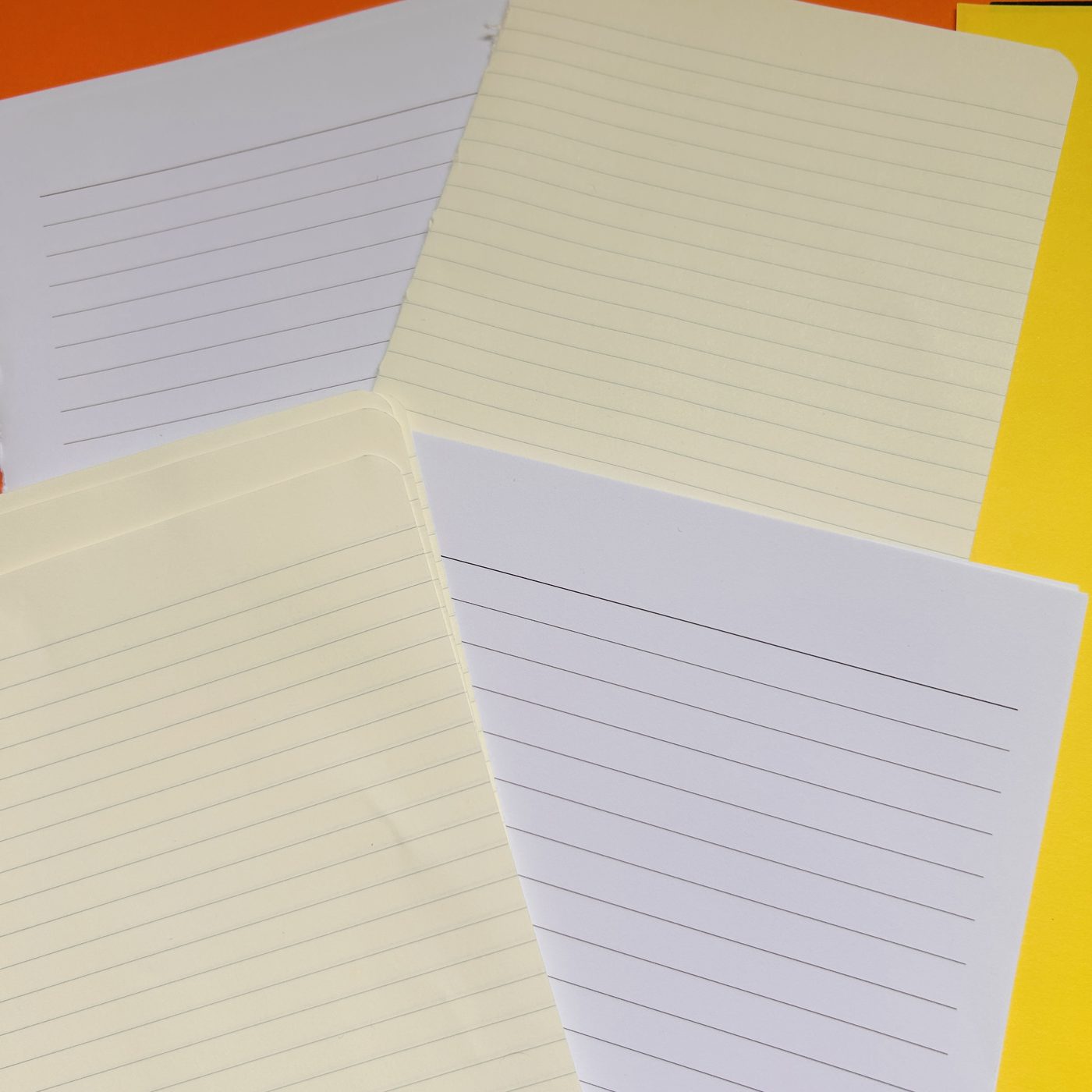 Blank and lined writing papers &mdash; a mix of cream and white lined sheets fanned out over orange and yellow card